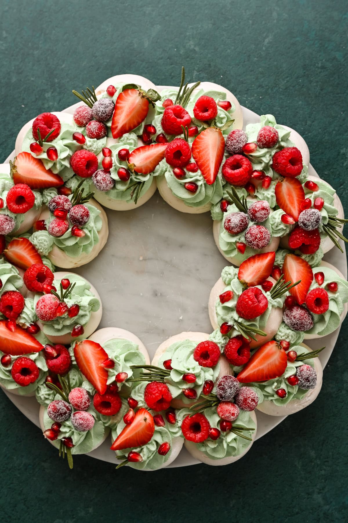 Meringue wreath topped with green whipped cream and red fruits.