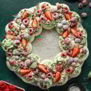 Overhead view of meringue wreath with green whipped cream, red fruit and powdered sugar.