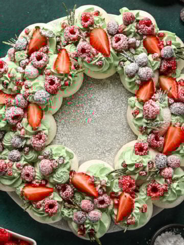 Overhead view of meringue wreath with green whipped cream, red fruit and powdered sugar.
