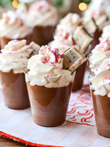 Peppermint Espresso martini pudding shots with whipped cream and christmas tree in background.