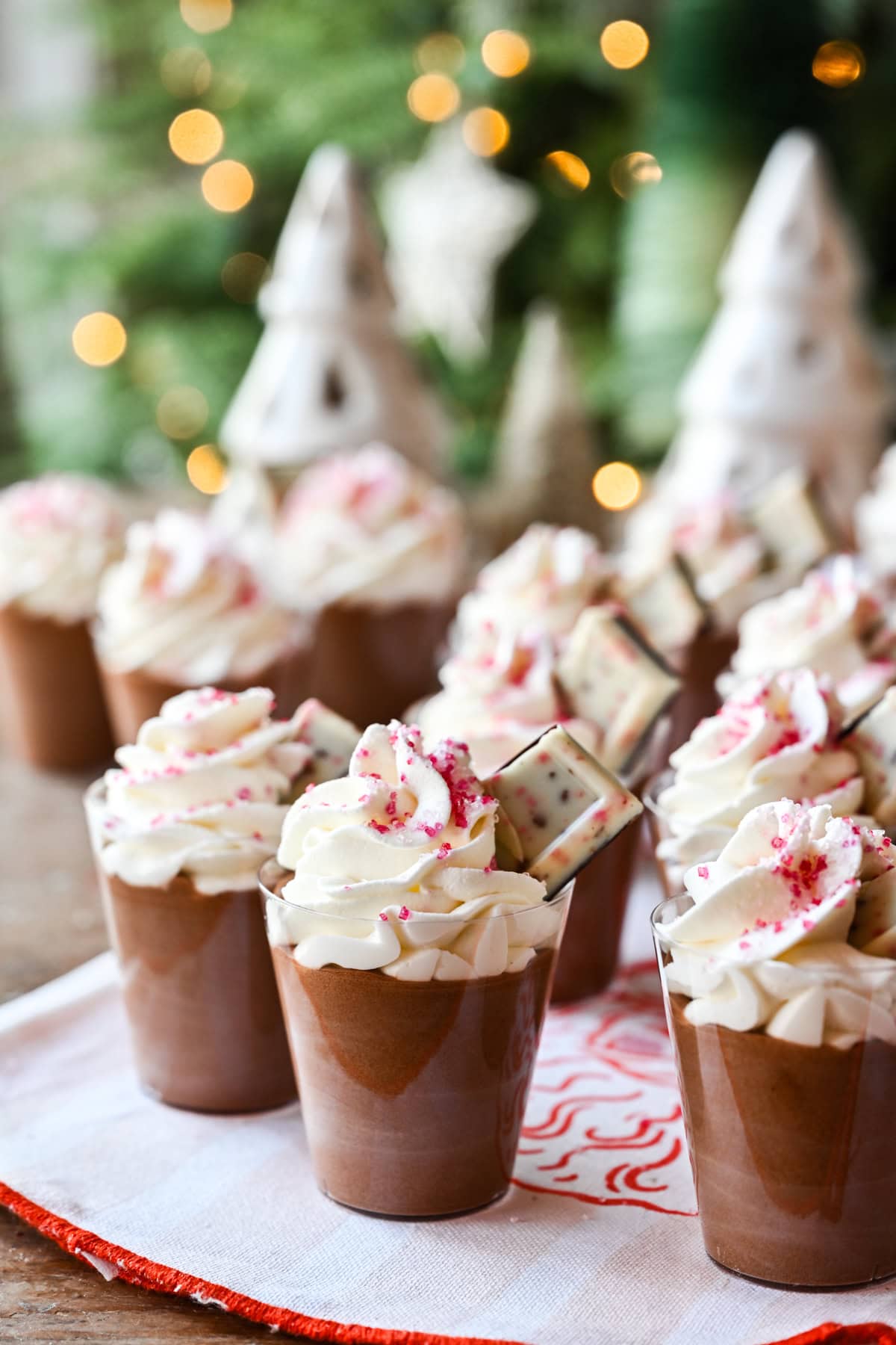Peppermint Espresso martini pudding shots with whipped cream and christmas tree in background.