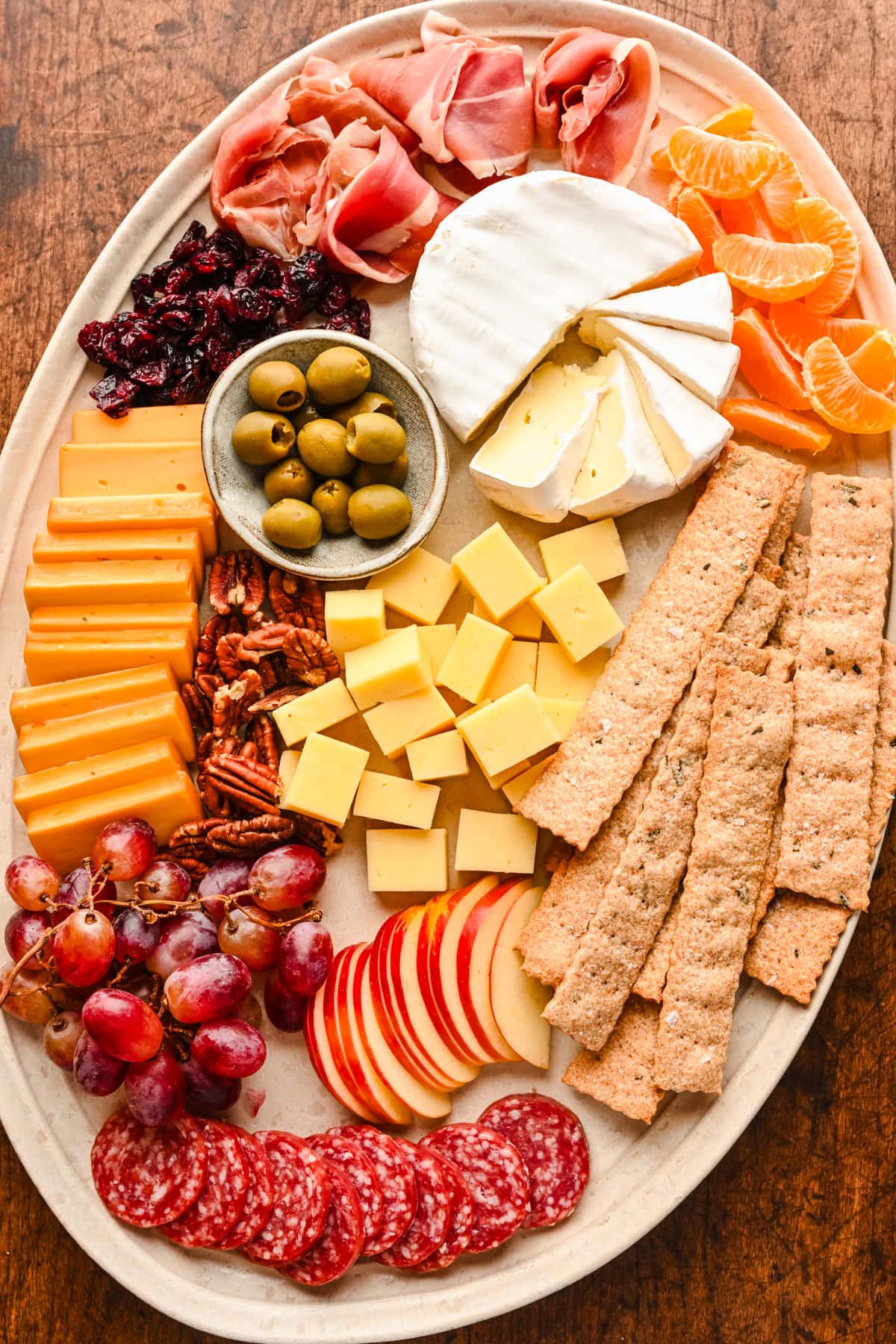 Charcuterie board featuring crackers apples cheese and grapes.