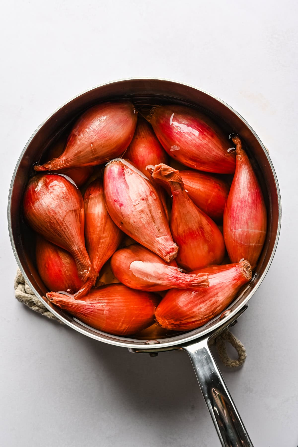 overhead view of whole shallots in a pot of water.