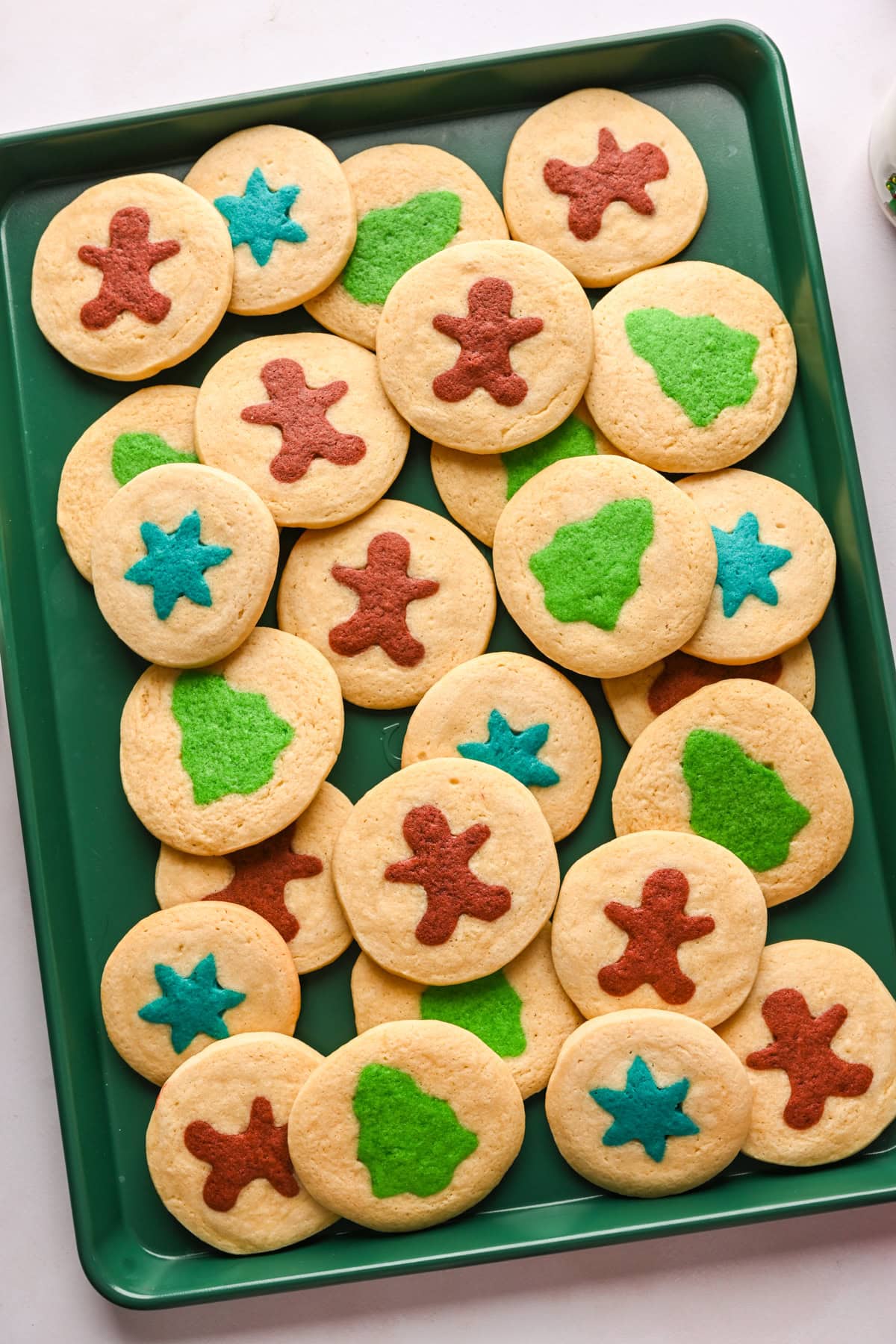 Overhead view of a cookie sheet with gingerbread men, snowflake and tree slice and bake cookies.