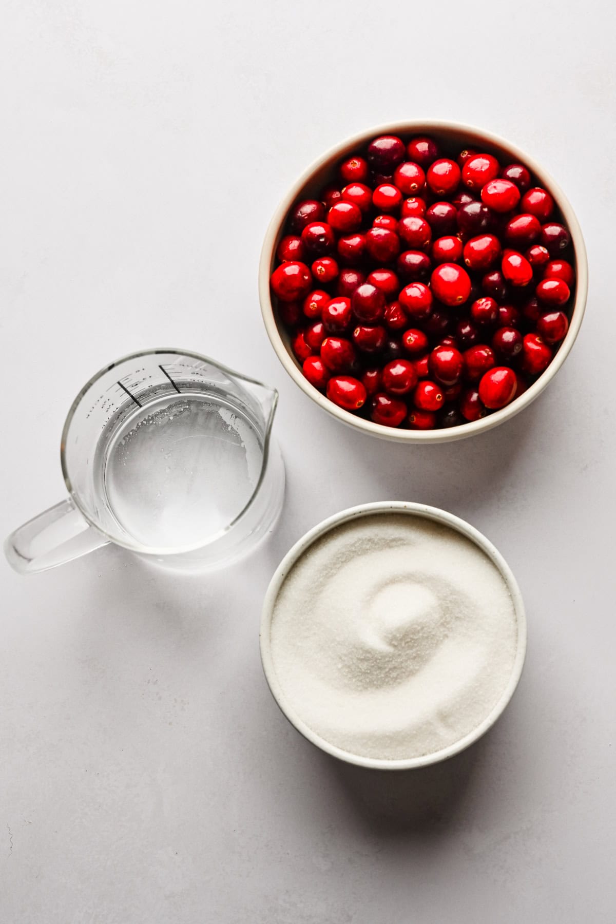 Fresh cranberries, water and sugar on a white backdrop.