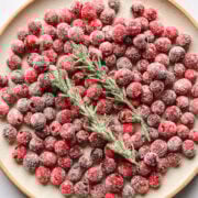 Frozen red currants with a sprig of rosemary on a white plate.