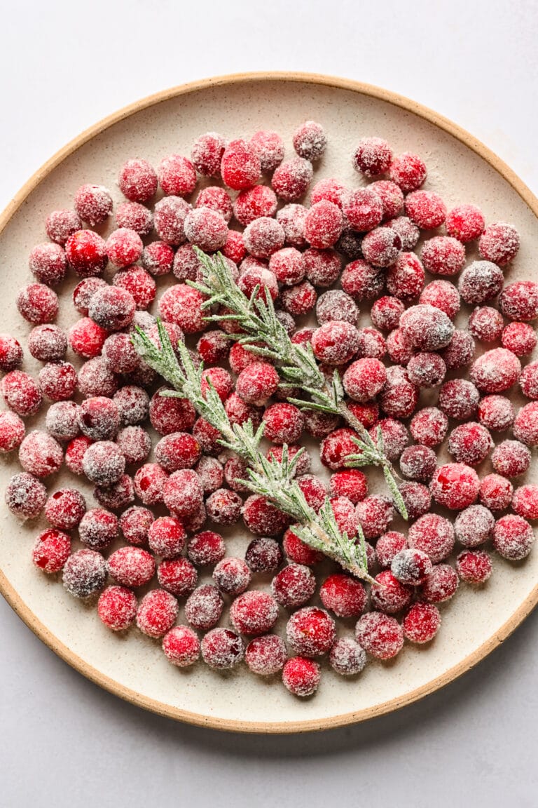 Frozen red currants with a sprig of rosemary on a white plate.