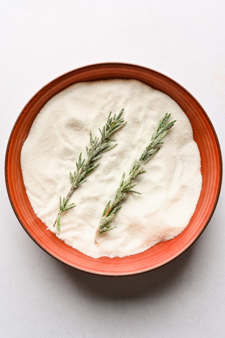Sugared rosemary in a bowl of sugar.