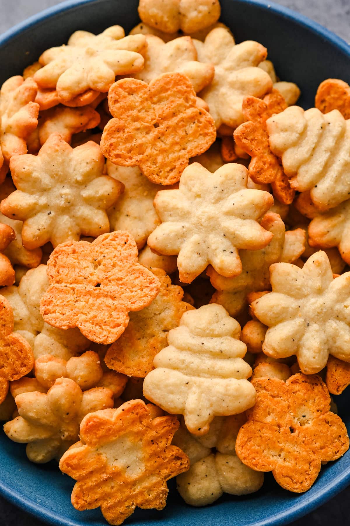 Close up view of White Cheddar Parmesan Spritz crackers in a blue bowl. 
