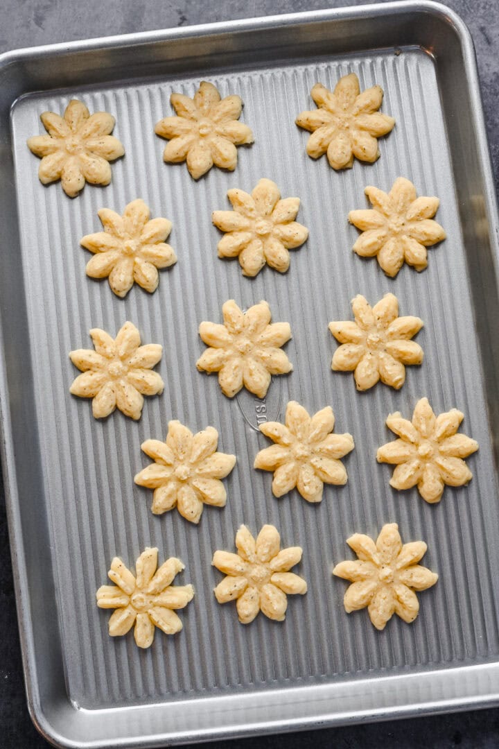 White cheddar spritz crackers in snowflake shape on cookie sheet before baking.