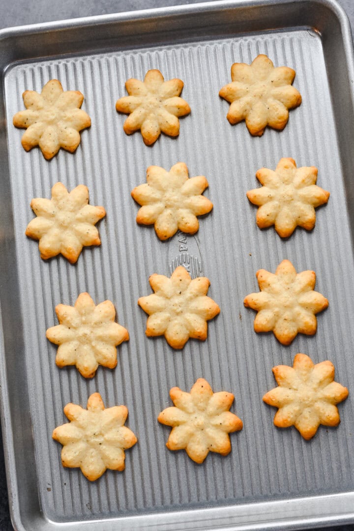 White cheddar spritz crackers in snowflake shape on cookie sheet after baking.