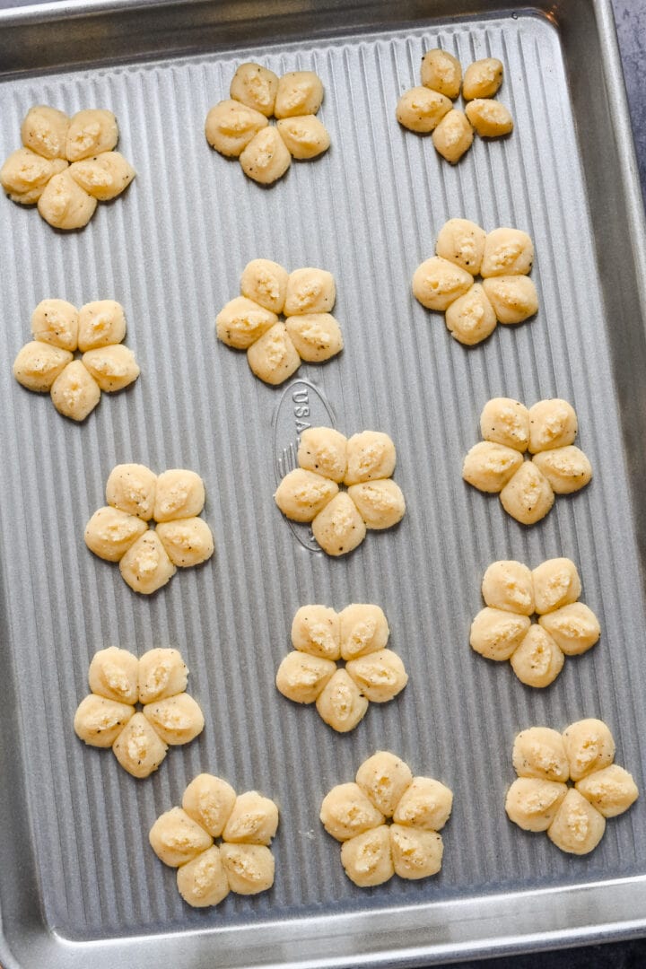 White cheddar spritz crackers in flower shape on cookie sheet before baking.