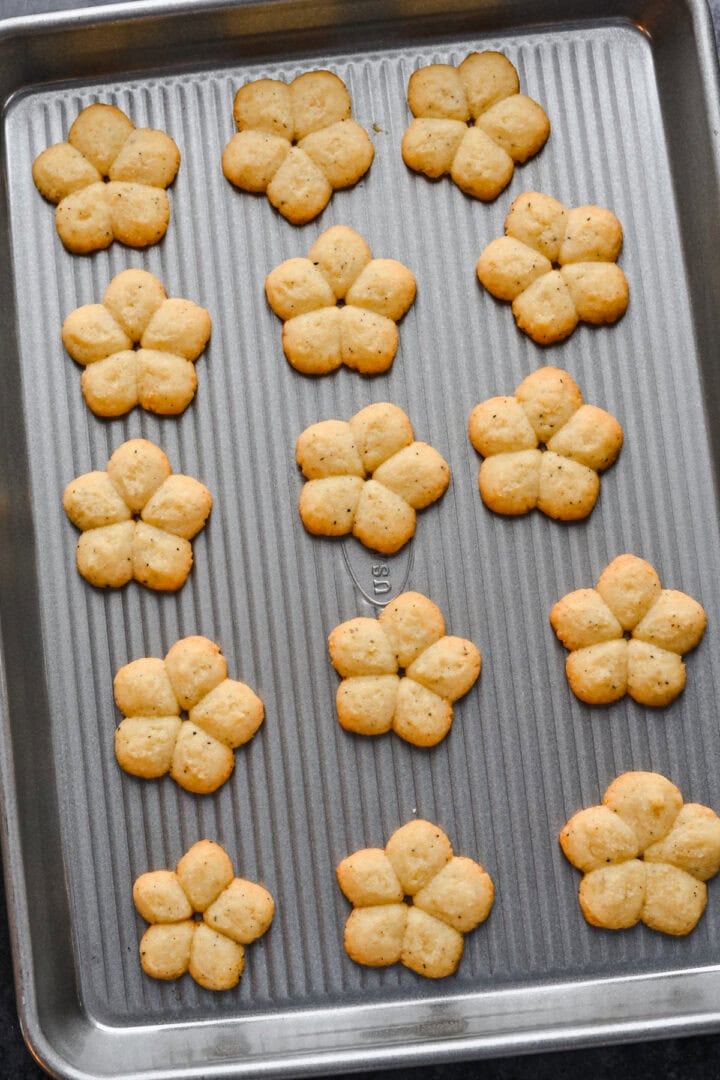 White cheddar spritz crackers in flower shape on cookie sheet after baking.