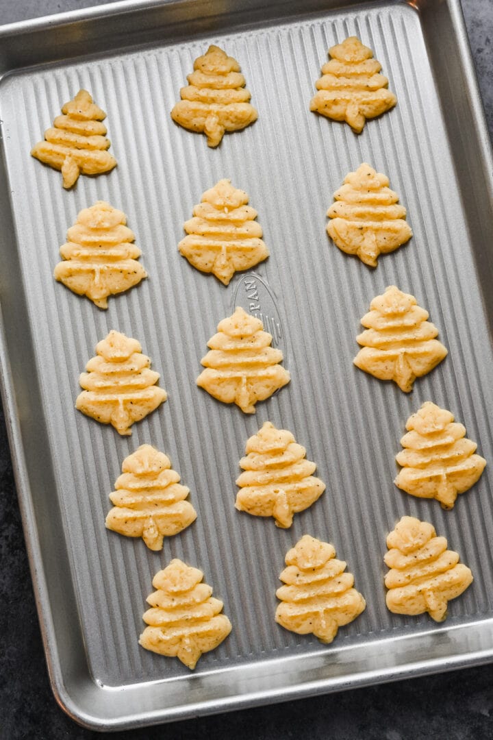 White cheddar spritz crackers in tree shape on cookie sheet before baking.