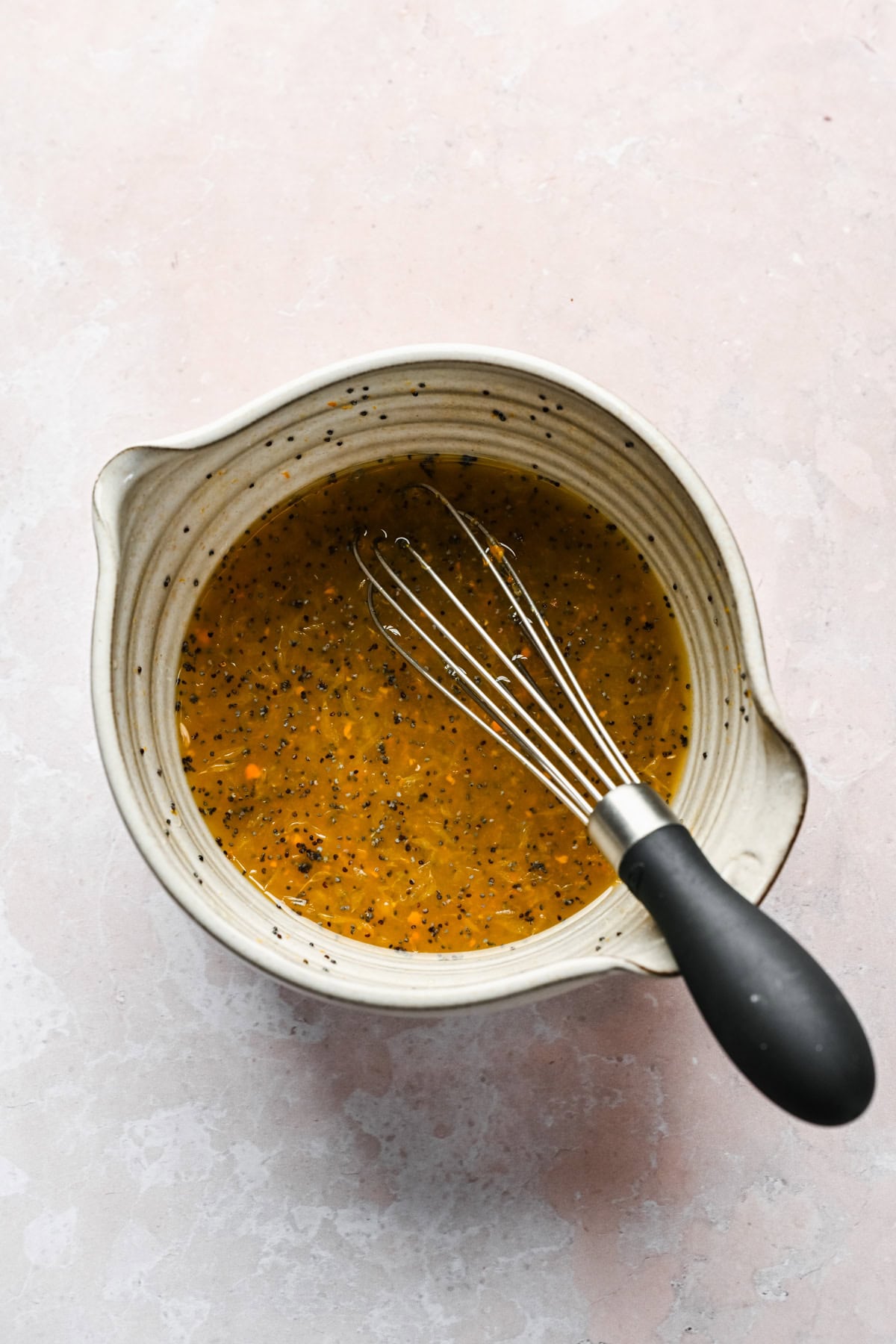 Overhead view of orange poppyseed dressing in small bowl with whisk.
