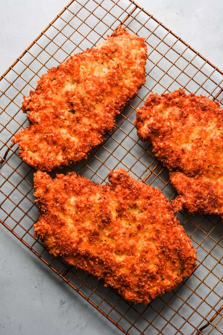 Overhead view of chicken cutlets on a wire rack.