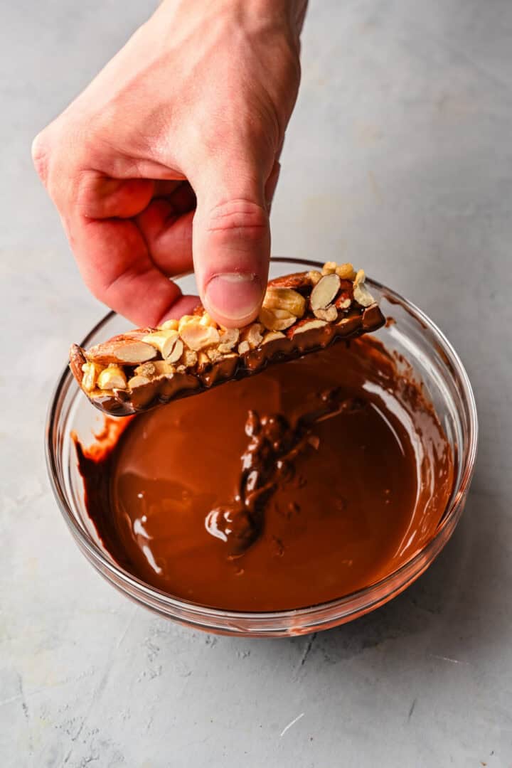 Dipping nut bar in chocolate.