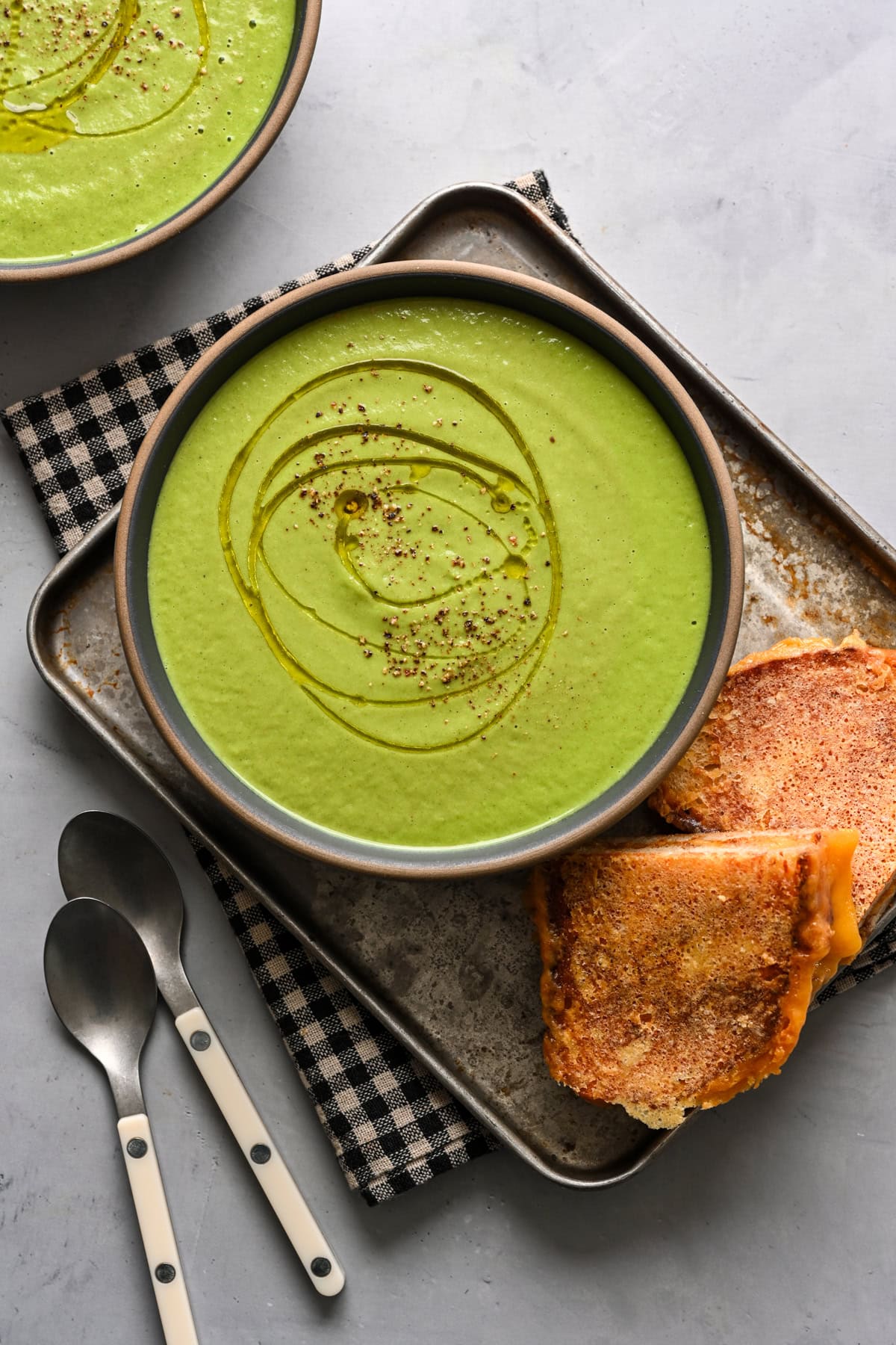 Overhead view of broccoli soup in a bowl alongside grilled cheese.