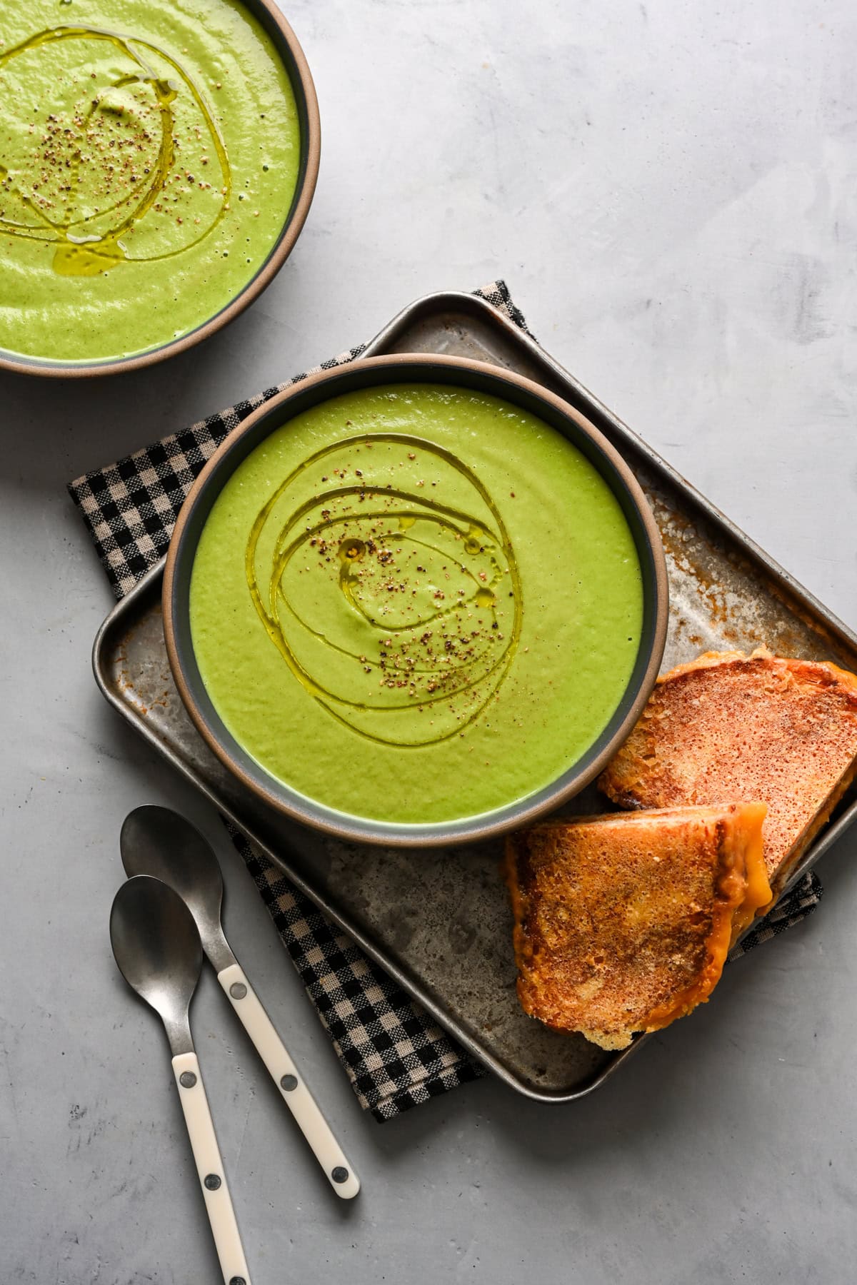 Overhead view of broccoli soup in a bowl alongside grilled cheese.