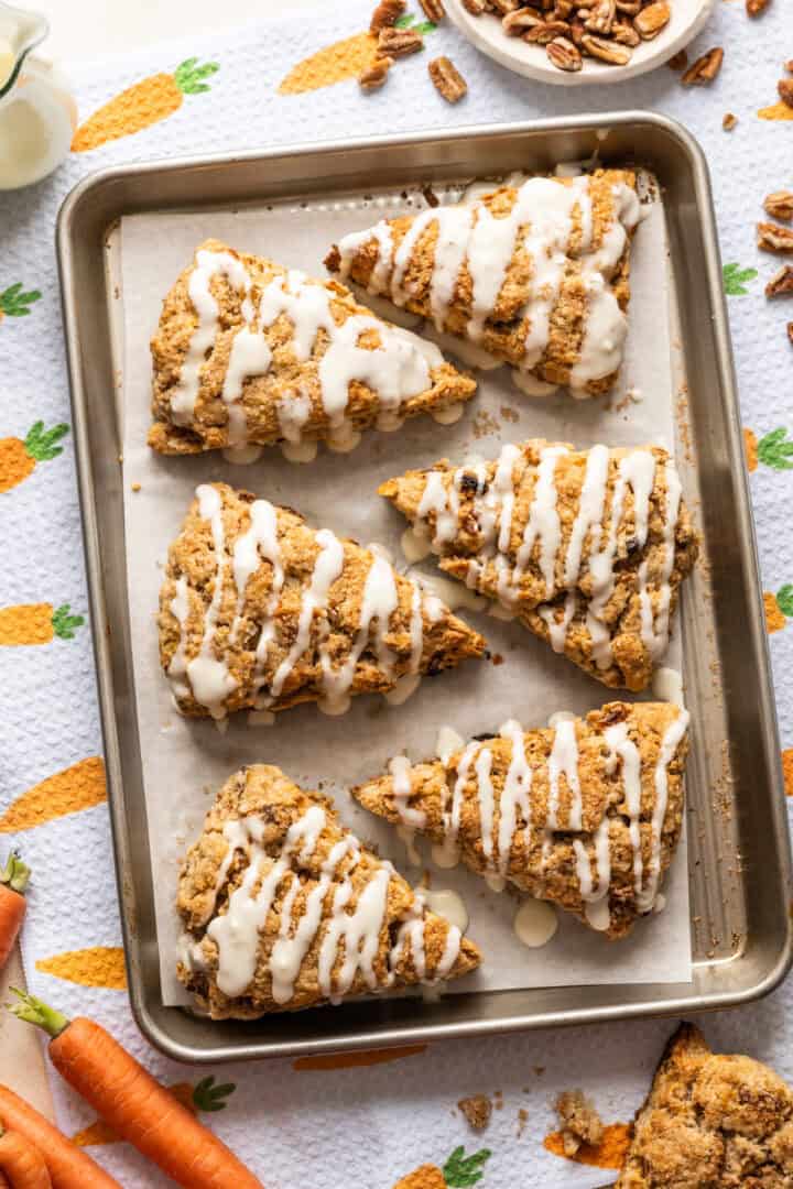 Carrot cake scones with cream cheese glaze drizzled on top on baking sheet.
