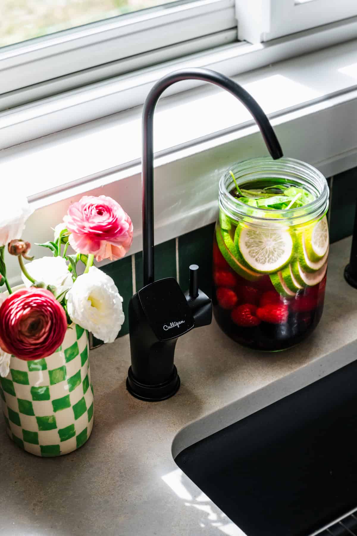 Reverse osmosis tap installed into countertop next to a vase of flowers and jar of infused water.