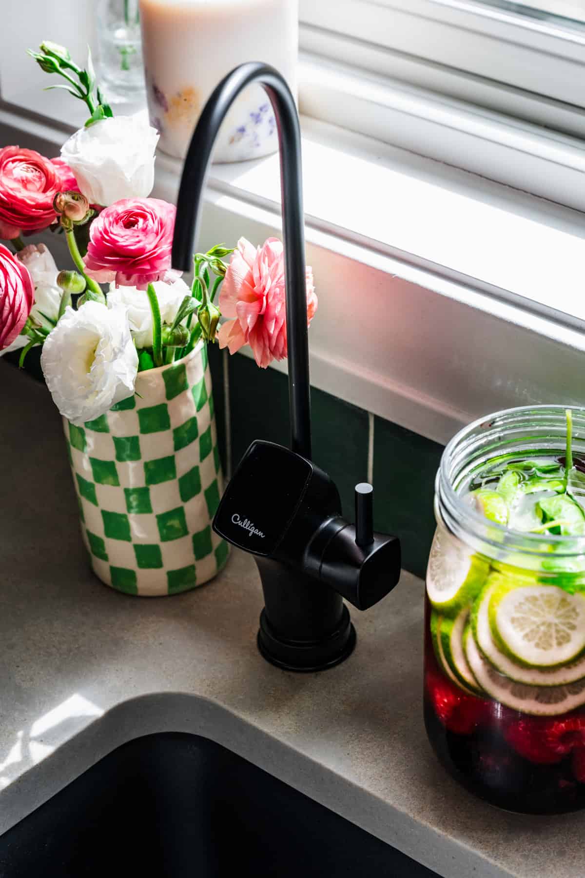 Reverse osmosis tap installed into countertop next to a vase of flowers and jar of infused water. 