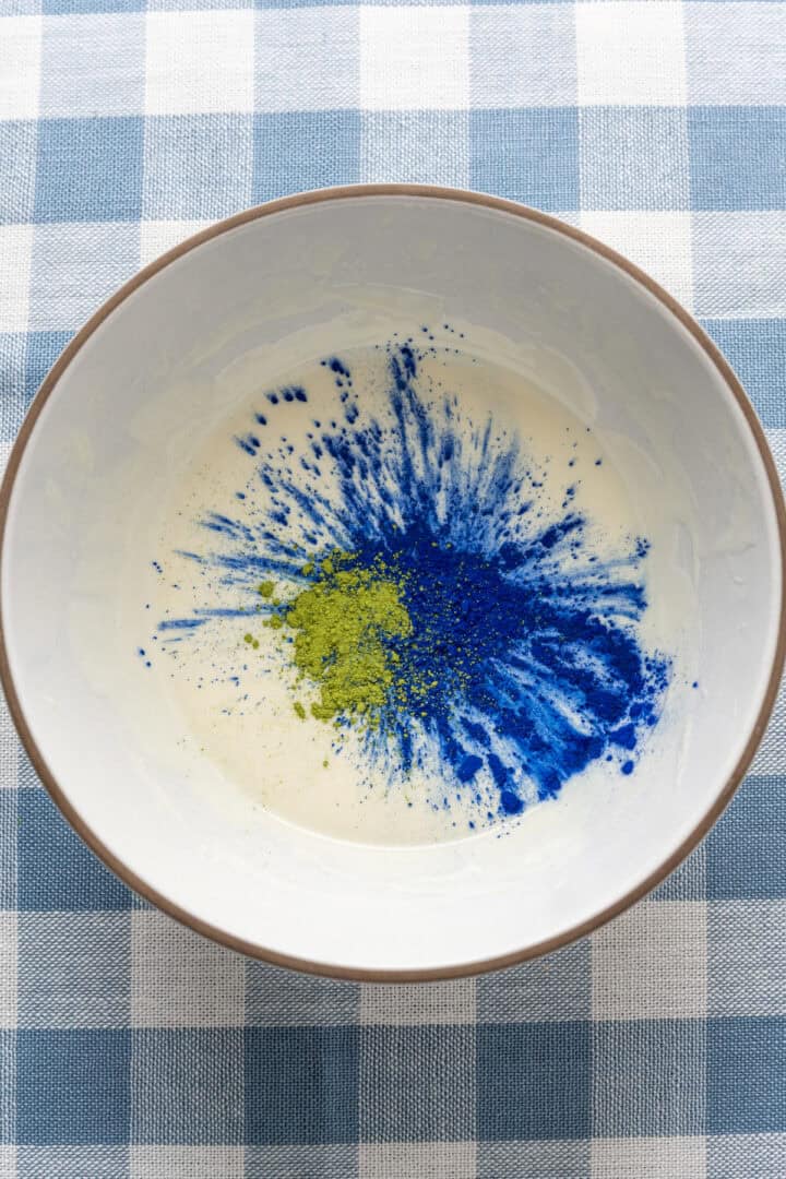 melted white chocolate in a bowl with blue spirulina powder and matcha powder.