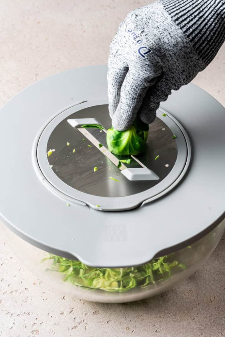 person shredding brussels sprouts on a slicer wearing a cut proof glove.