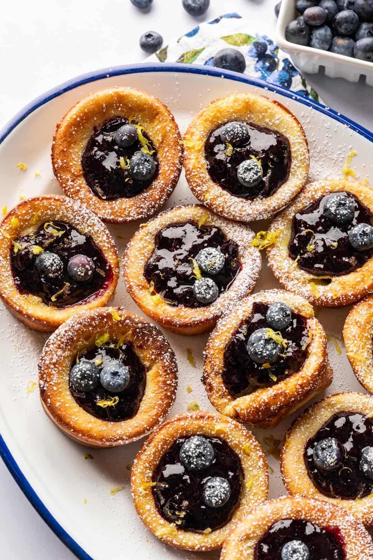 45 degree angle view of mini dutch baby pancakes on a platter filled with blueberry lemon compote.