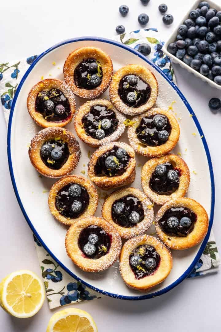 Overhead view of mini dutch baby pancakes on a platter filled with blueberry lemon compote.