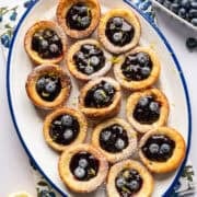 Overhead view of mini dutch baby pancakes on a platter filled with blueberry lemon compote.