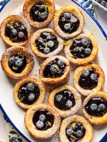 Overhead view of mini dutch baby pancakes on a platter filled with blueberry lemon compote.
