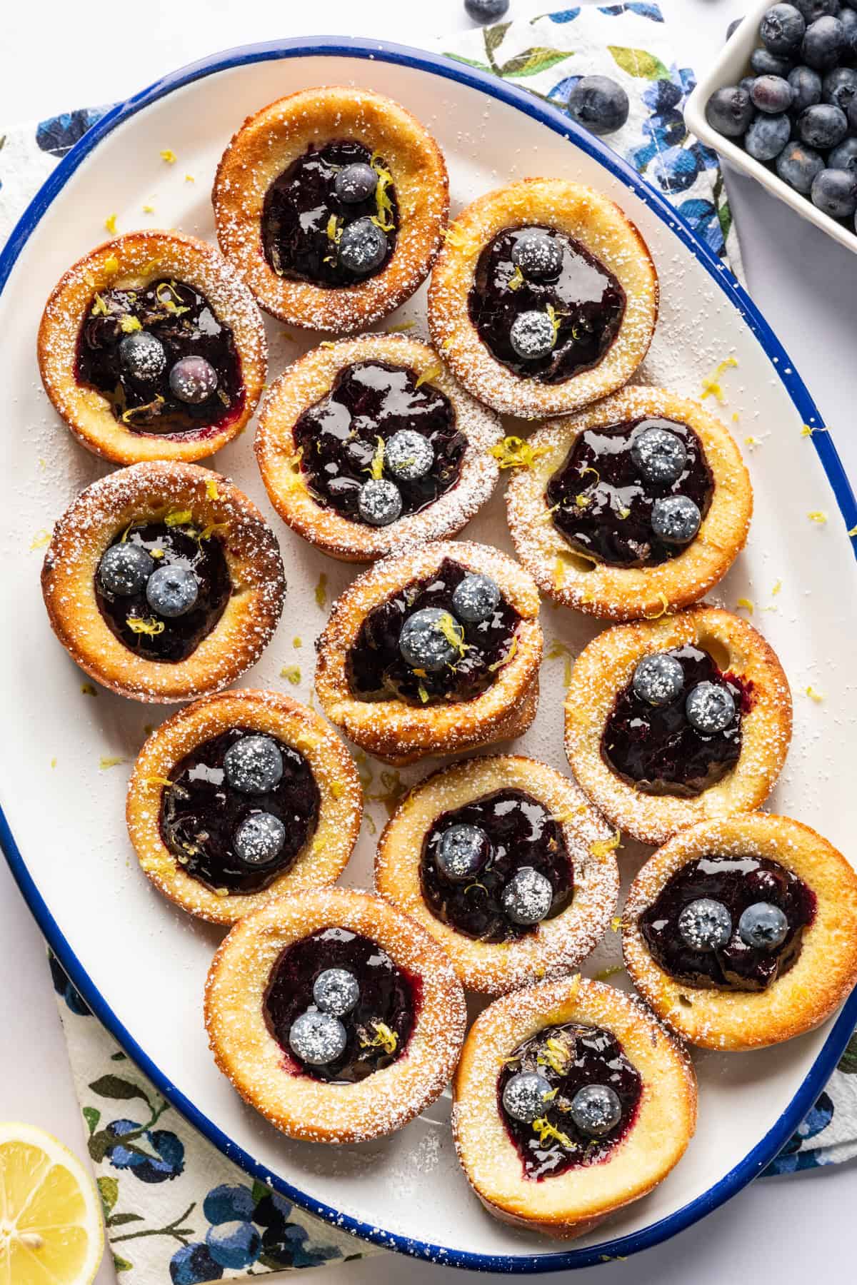 Overhead view of mini dutch baby pancakes on a platter filled with blueberry lemon compote. 