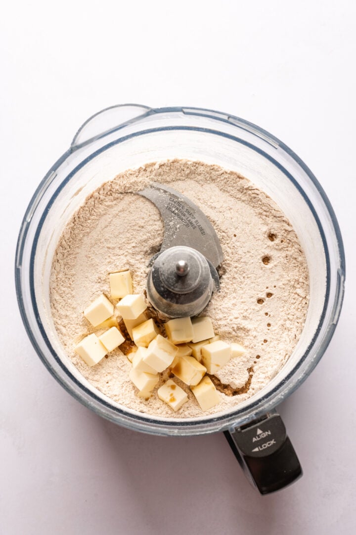 overhead view of dry ingredients and cubed butter in a food processor. 