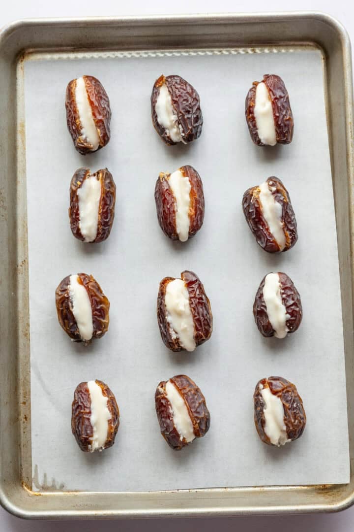 12 medjool dates stuffed with coconut butter on parchment paper. 