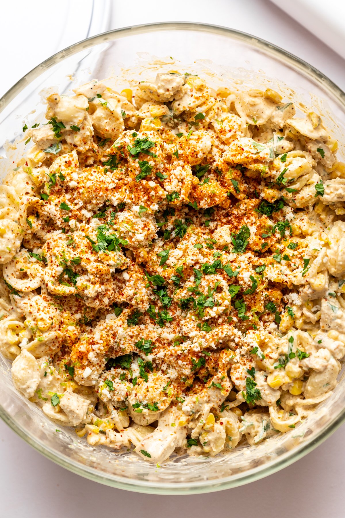 Overhead view of elote pasta salad with grilled chicken in large glass bowl.