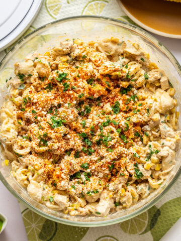 Overhead view of elote pasta salad with grilled chicken in large glass bowl.