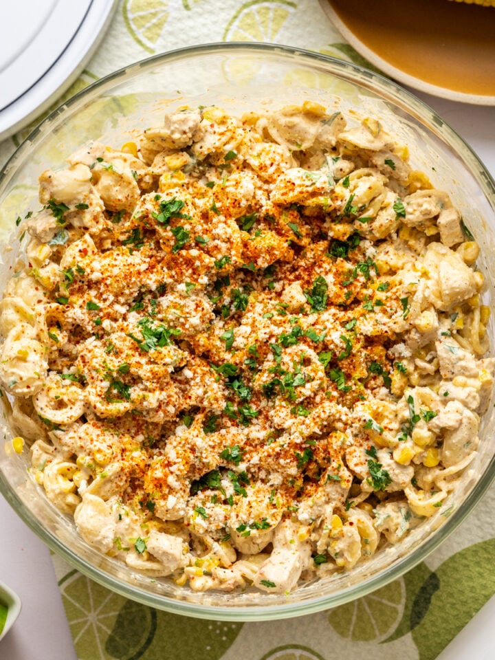 Overhead view of elote pasta salad with grilled chicken in large glass bowl.