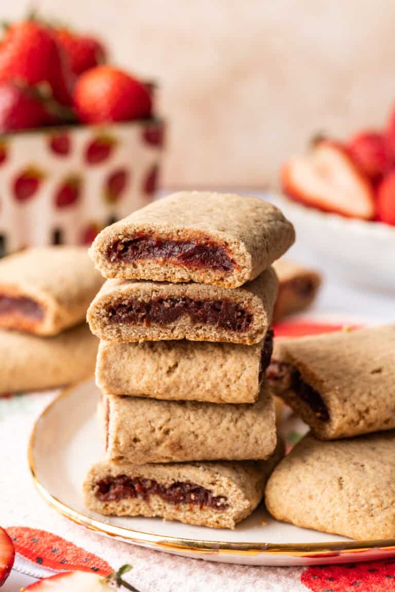 Golden baked strawberry chocolate cookies stacked on a plate with fresh strawberries in the background.