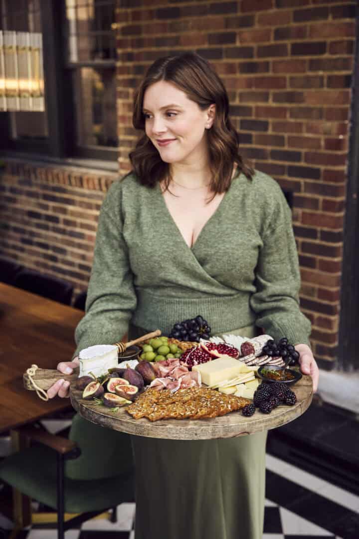 Lexi from crowded kitchen holding a charcuterie board.