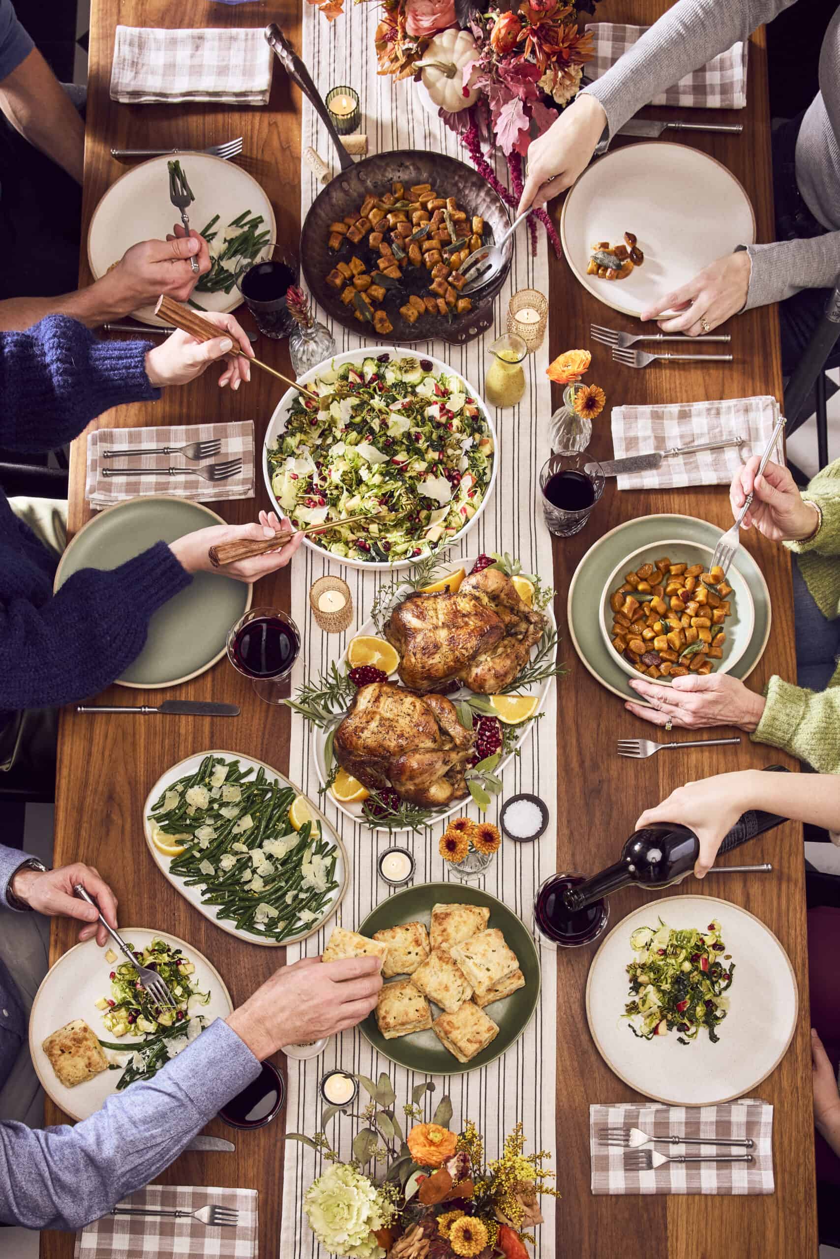 overhead view of fall dinner tablescape with hands reaching in and serving food.
