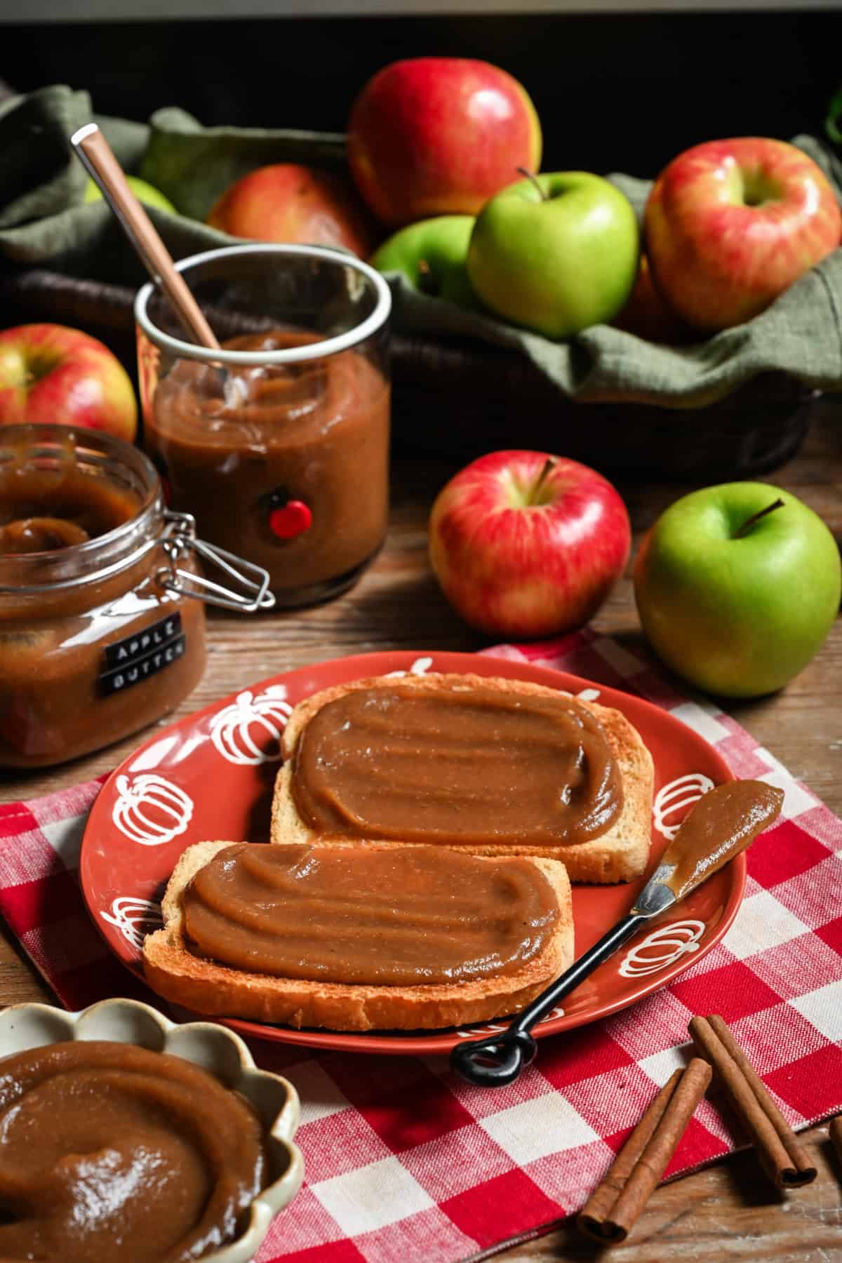 Apple butter spread onto toast on orange plate with apples in the background. 