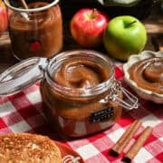 Close up view of apple butter in a jar with apples in the background.