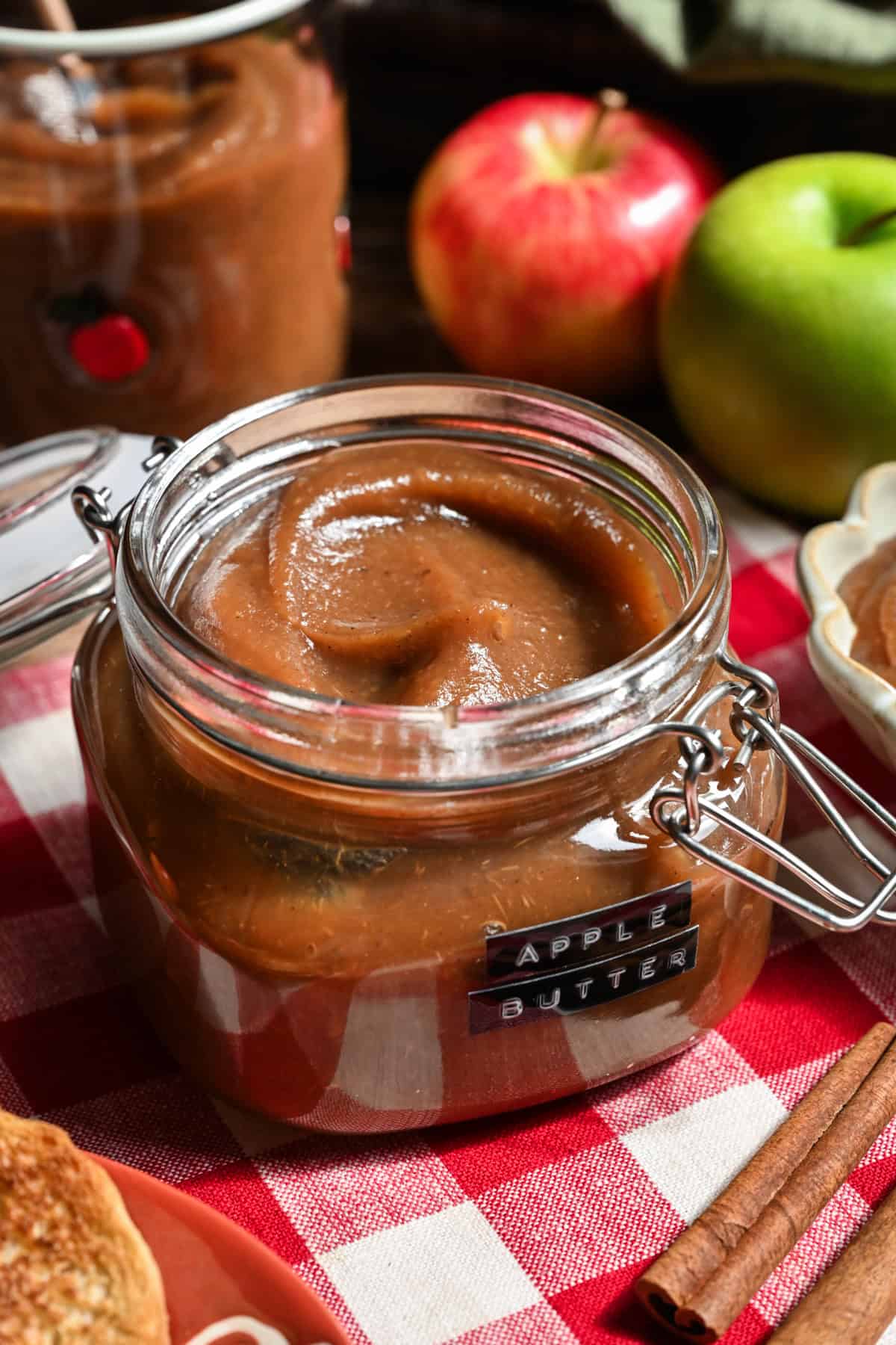 Close up view of apple butter in a jar with apples in the background. 