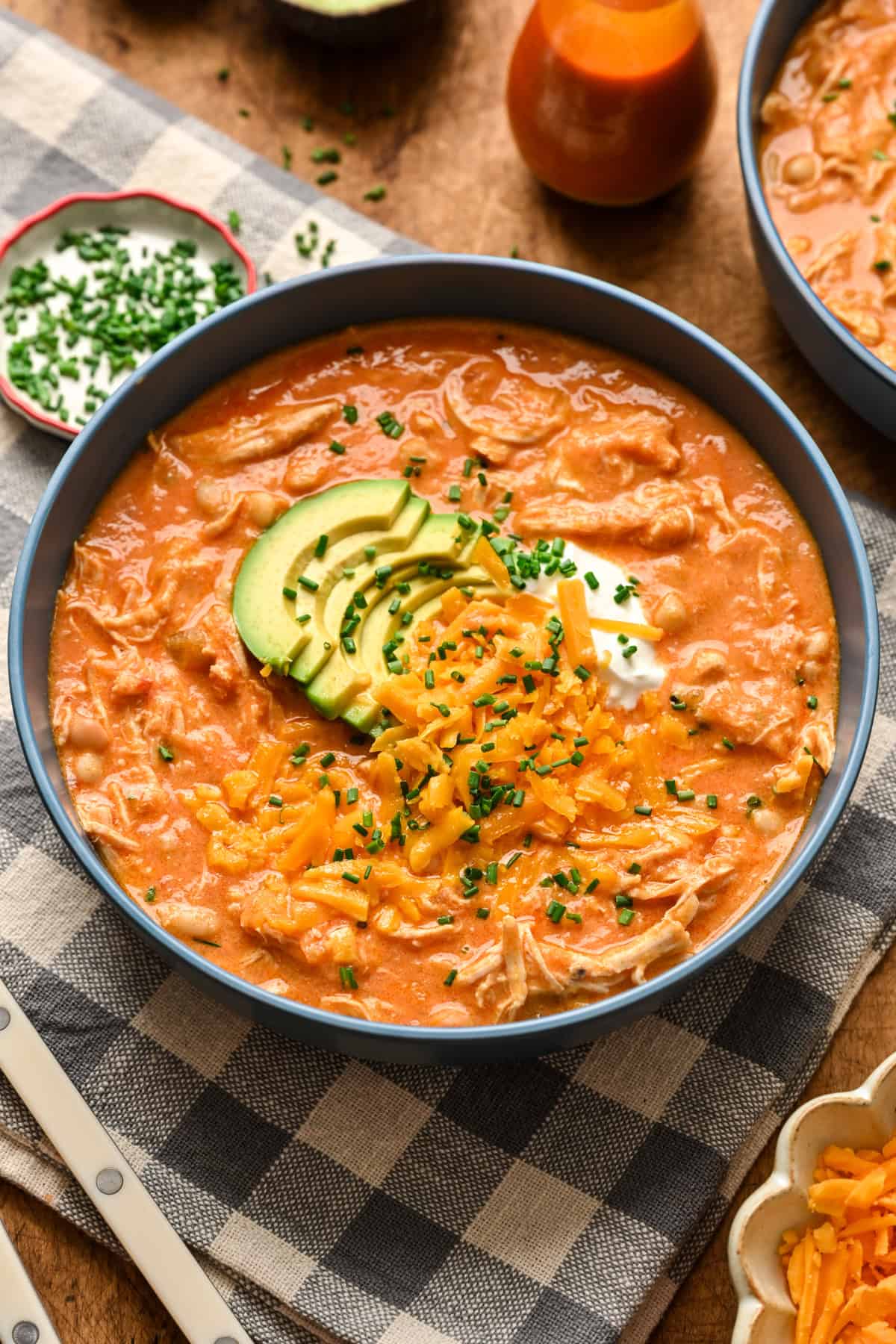 45 degree angle view of creamy buffalo chicken chili topped with avocado, cheddar cheese and sour cream. 
