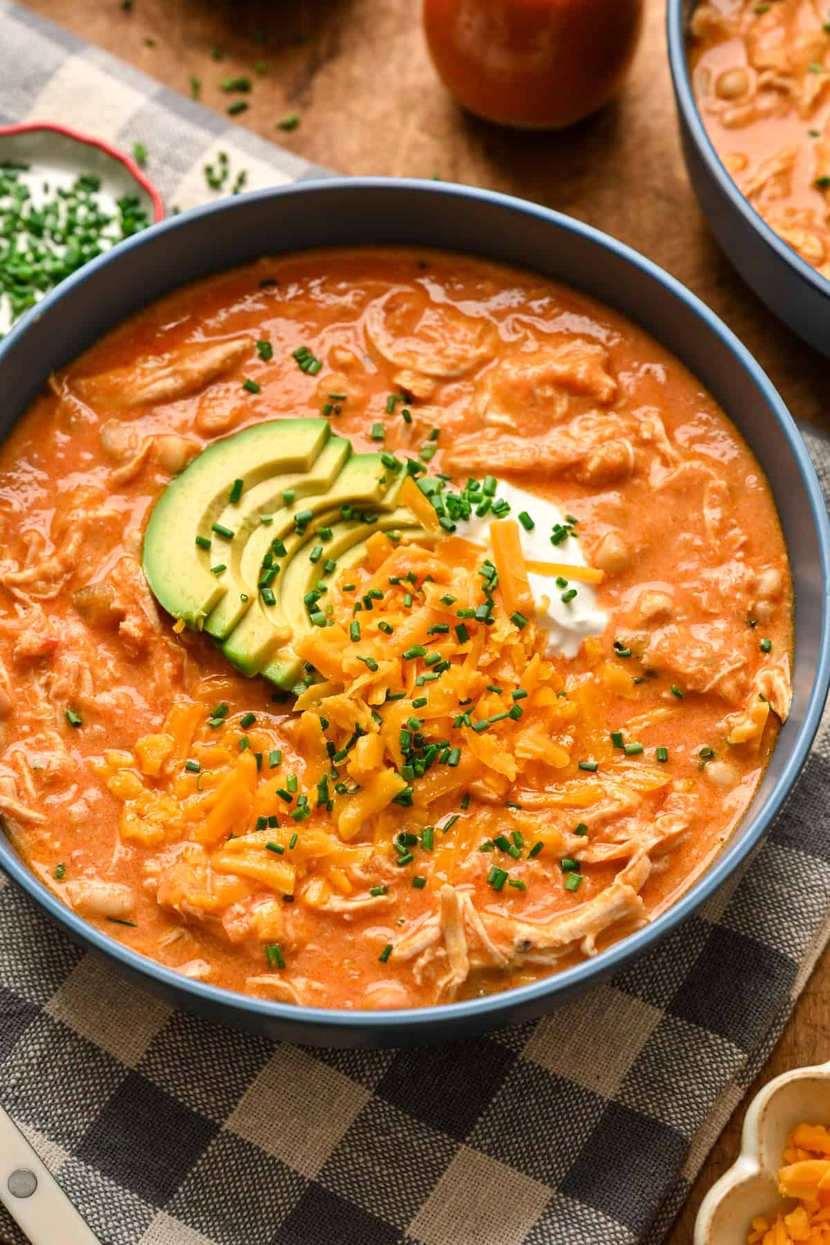 45 degree angle view of creamy buffalo chicken chili topped with avocado, cheddar cheese and sour cream.
