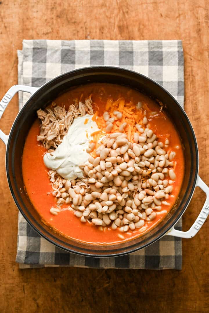Buffalo chicken chili in a pot with beans, sour cream, cheese and shredded chicken before stirring. 