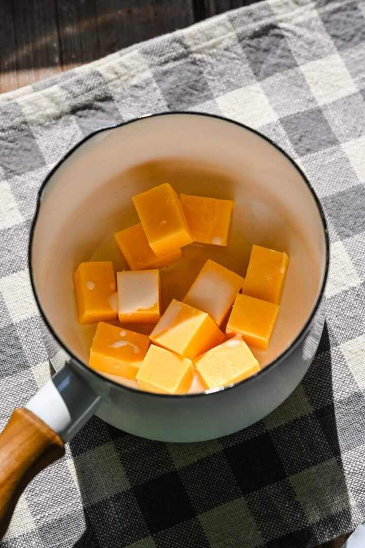 Cheddar cheese cubes and milk in pot before melting.