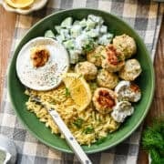 Close up view of feta chicken meatballs in a green bowl with orzo, cucumbers and a dill yogurt sauce.