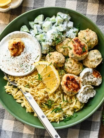 Close up view of feta chicken meatballs in a green bowl with orzo, cucumbers and a dill yogurt sauce.